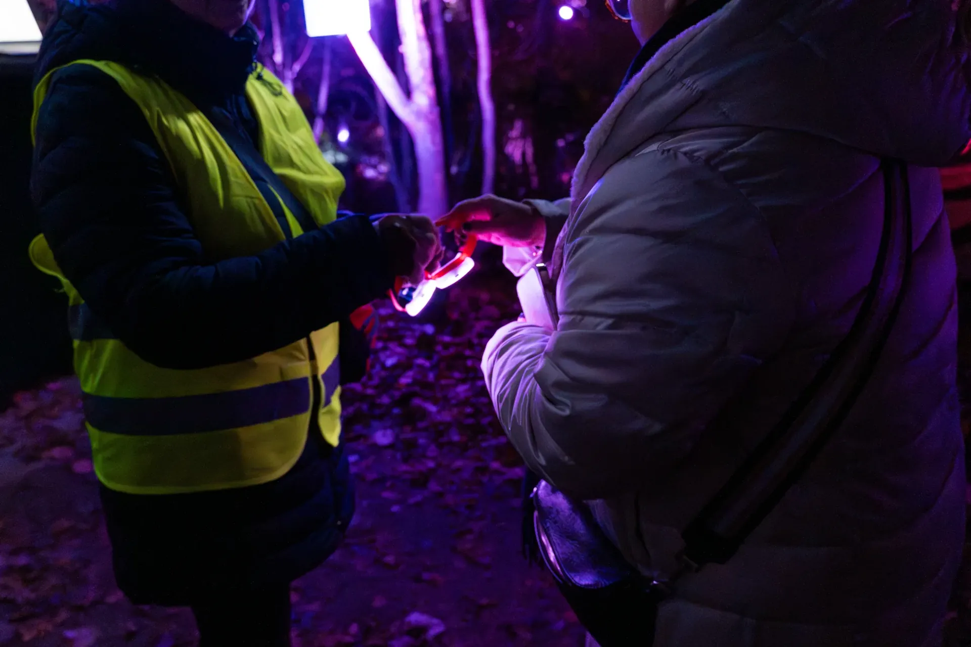 Steward in fluovest overhandigt een oplichtende LED-armband aan een gast, in paars avondlicht